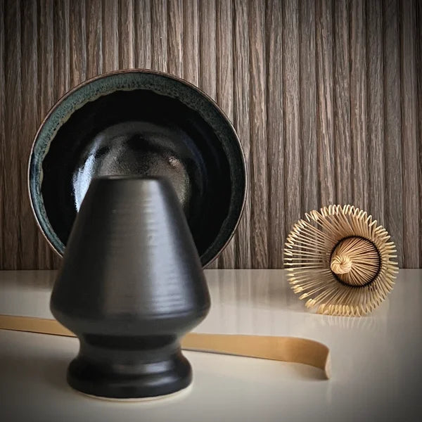 Matcha set met zwarte matcha kom, inclusief bamboe matcha klopper, bamboelepel en zwarte whiskhouder op voorgrond.